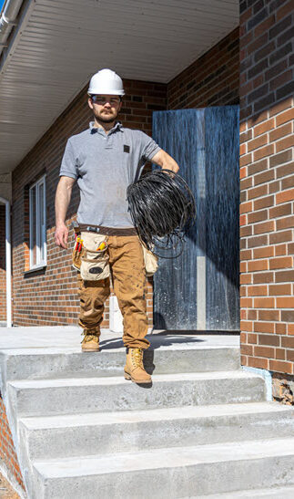 Construction worker carrying coiled wire outside brick building.